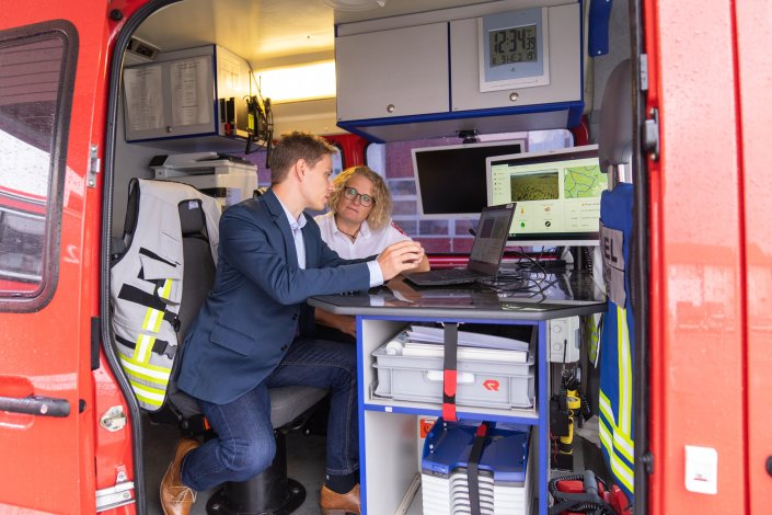 Female and male person sitting in the fire engine with the door open and discussing something in front of a laptop